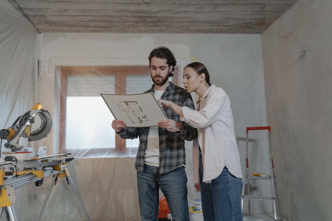 about-bg Man and woman reviewing floor plans in a home renovation setting, discussing project details.