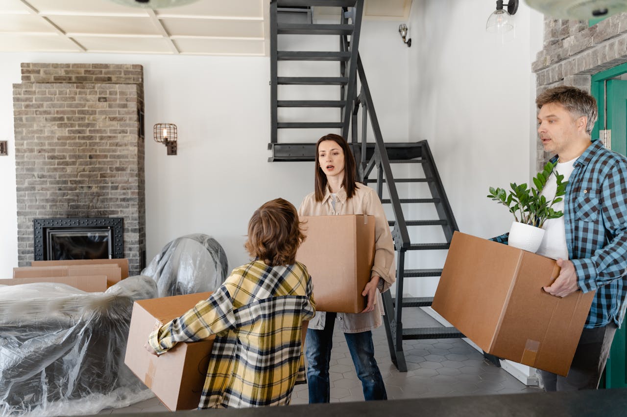 services-03 A family carrying boxes and a plant while moving into a new home with an industrial-style interior.